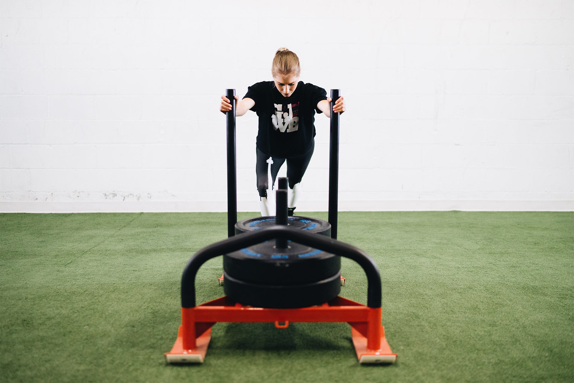 A women in workout clothes pushing a weighted sled