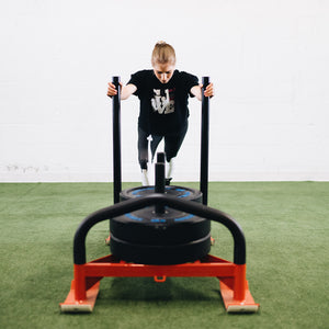 A women in workout clothes pushing a weighted sled