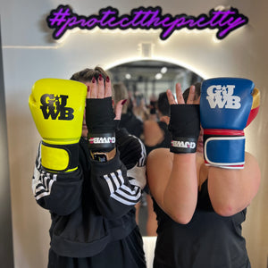 2 girls holding hands up with one hand having a black handwrap and the other with a boxing glove on 