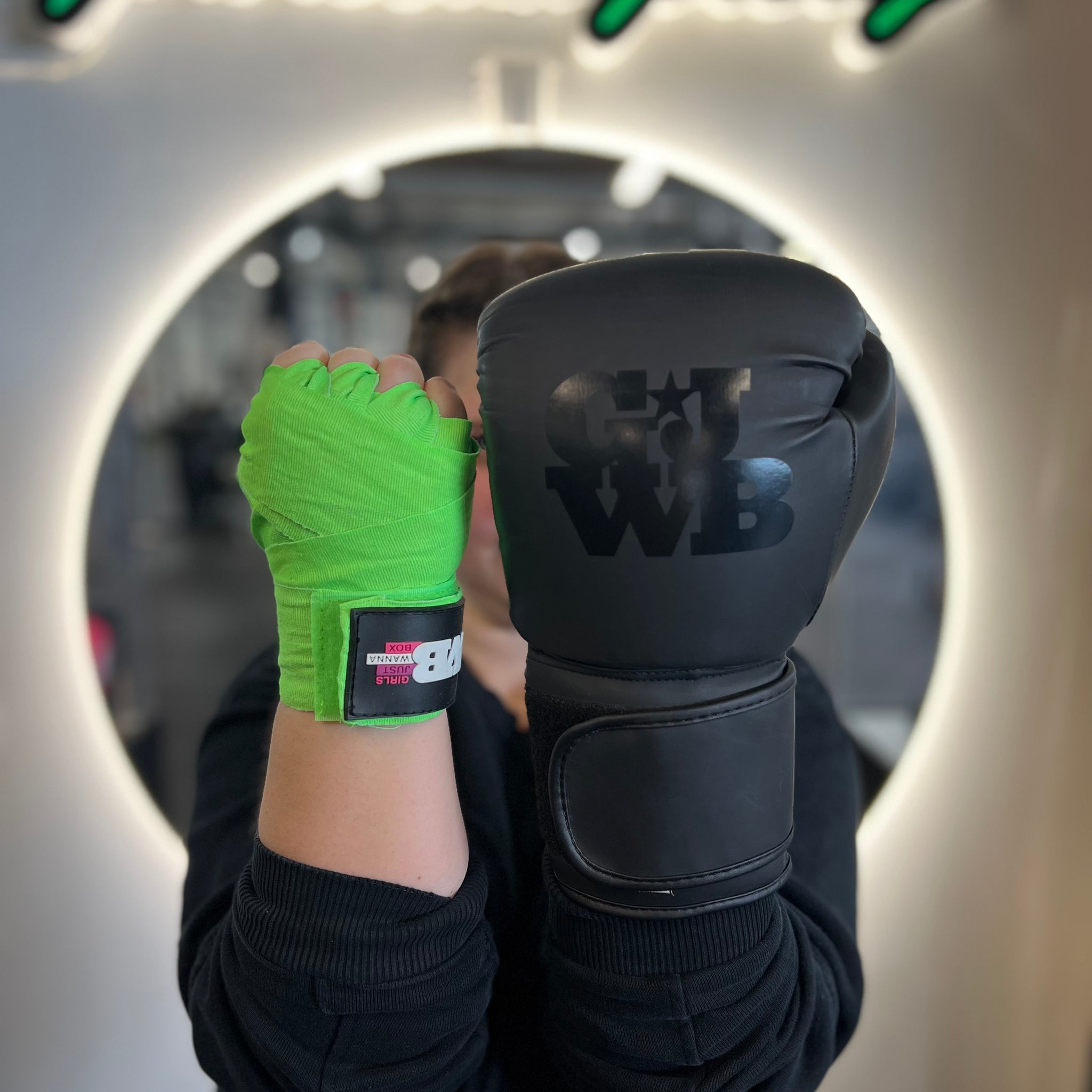 a girls holding hands up with one hand having a neon green handwrap and the other with a boxing glove on 