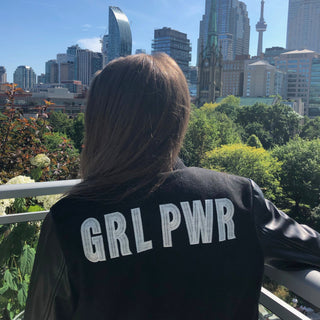 girl with a view of city skline wearing a GRL Power varsity vegan leather jacket